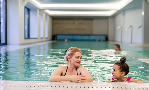 Mutter und Tochter in Badeanzügen am Beckenrand der Sporthalle. Sie sehen glücklich, modisch und fit aus. — Stockfoto