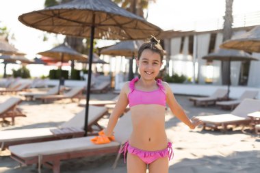 little girl on the sandy beach with straw umbrellas