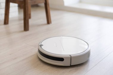 Akıllı Ev. Elektrikli süpürge robotu oturma odasında ahşap zeminde koşar.