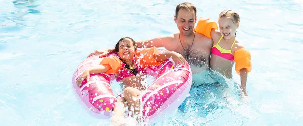 Aktif bir baba çocuklarına tropik tatil köyünde havuzda yüzmeyi öğretiyor. Yaz tatilleri ve spor konsepti