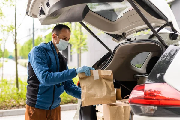 Man by the car. Guy in a delivery uniform. Man in a medical mask. Coronavirus concept.