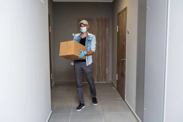 Házhozszállítás bevásárlókocsi férfi kesztyűben és védőmaszkban csomagokat szállít az ajtónál — Stock Fotó