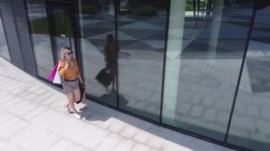 Happy female shopaholic is having fun in shopping mall with bright bags and shop windows.