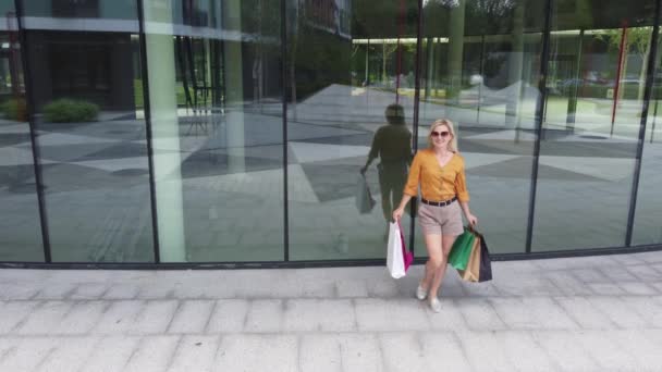 Happy female shopaholic is having fun in shopping mall with bright bags and shop windows. — Video