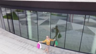 Happy female shopaholic is having fun in shopping mall with bright bags and shop windows.