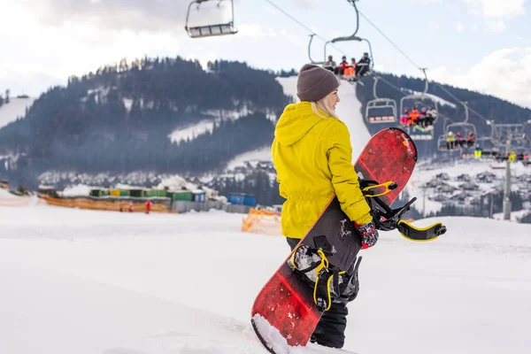 Jonge vrouw met snowboard op de helling van de heuvel in wintersportplaats — Stockfoto