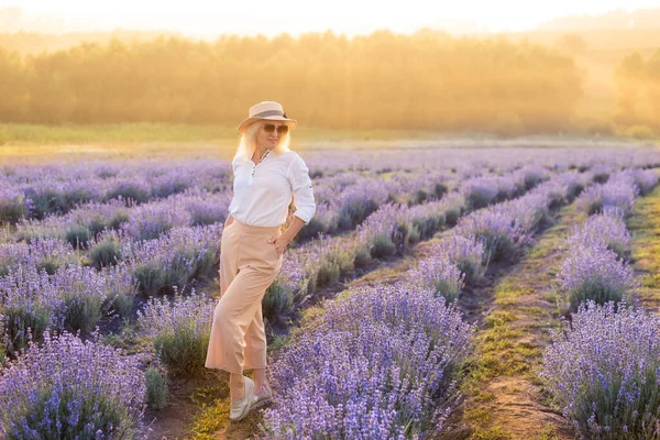 若いブロンドの女性旅行者はラベンダーの花で囲まれたラベンダー畑でわら帽子をかぶって. — ストック写真