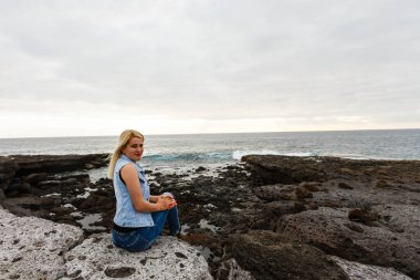 Volkanik kayalıklardaki kadınlar ve dalgalı mavi okyanus, beyaz köpük ve volkanik kayalar. Kanarya Adaları. Atlantik Okyanusunun muhteşem kıyıları