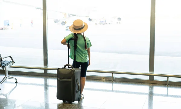 การท่องเที่ยว, วันหยุด, วัยเด็กและการขนส่ง แนวคิด - สาวน้อยที่ยิ้มพร้อมกระเป๋าเดินทาง, ตั๋วและพาสปอร์ตเหนือพื้นหลังสนามบิน . — ภาพถ่ายสต็อก