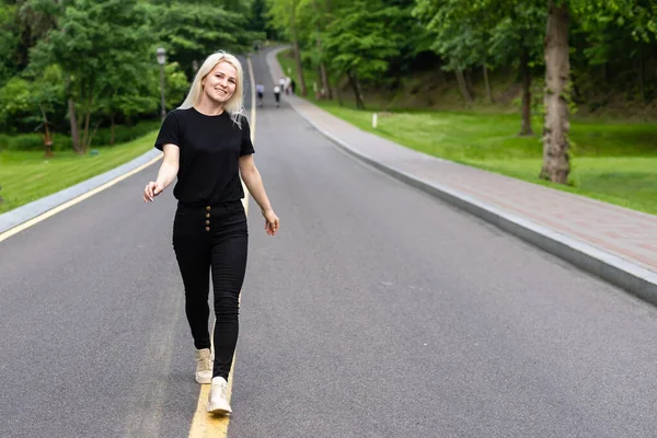 Jovem mulher atraente caminha ao longo da linha da estrada apreciando a natureza. — Fotografia de Stock