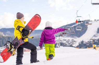 Snowboard yapan anne ve kızı karda oynuyorlar.