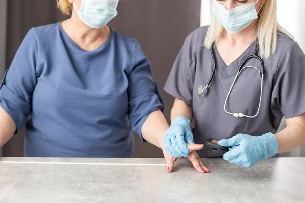 Medizinische Hilfe zu Hause. Ärztin in medizinischer Maske misst Puls und Sauerstoffsättigung der Patientin mittleren Alters mit einem Pulsoximeter im Sitzen auf dem Sofa, Gesundheitskonzept — Stockfoto