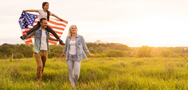 Vacker familj med den amerikanska flaggan i ett fält vid solnedgången. Självständighetsdagen den 4 juli. — Stockfoto