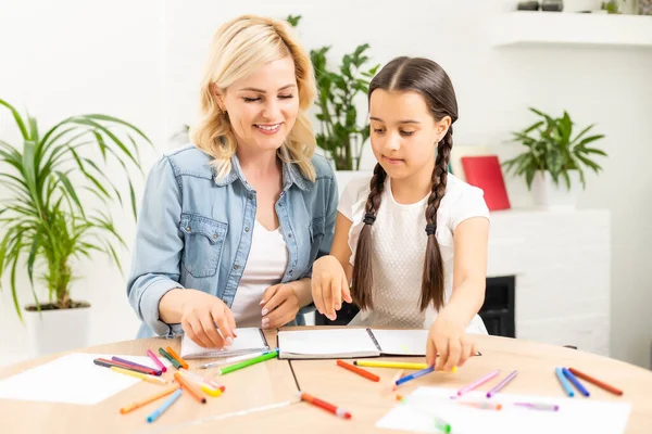 Moeder en dochter mooi en gelukkig maken een kaart voor moeders dag zitten samen aan tafel met papier en potloden — Stockfoto