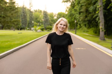 Günlük kıyafetlerle gezen neşeli genç bayan kırsal alanda asfalt yolda yürüyor, dışarıda otostop çekiyor. Güzel milenyum kadını otostop ile tek başına seyahat ediyor.