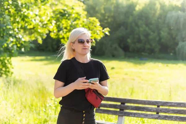 Portrait de belle jeune femme souriante en gros plan avec téléphone portable, sur fond de parc vert d'été. — Photo