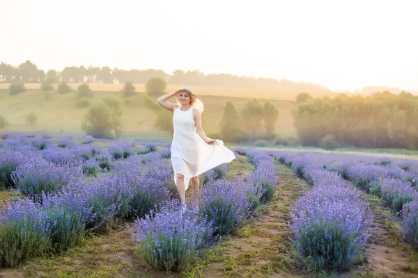 ラベンダー畑を歩いている美しい若い女性。ファッションドレス、わら帽子. — ストック写真
