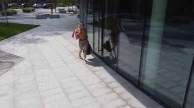 Alışveriş merkezinde elinde kağıt poşetlerle cam vitrinlere bakan mutlu kadın. Çekici, şık bir kadın. Sezonluk satışlarda kıyafetlere hayran gülümsüyor..