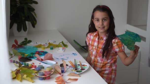 Close-up da menina sentada à mesa desenhando as folhas com pincel e aguarelas. menina pintando folhas caídas em casa. Outono — Vídeo de Stock