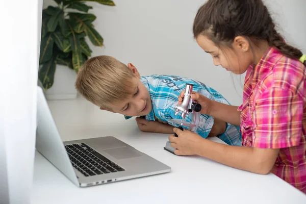 Jongen en meisje, broer en zus studeren thuis. Een meisje kijkt naar een videoles of een online conferentie, een jongen doet oefeningen in een notitieboekje uit een lesboek — Stockfoto