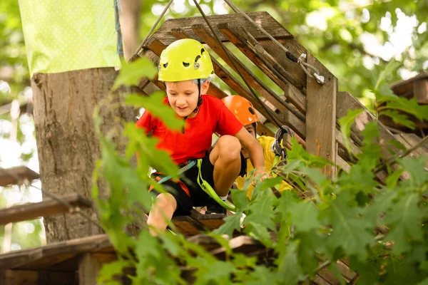 Bonito menino da escola desfrutando de um dia ensolarado em um parque de atividades de aventura de escalada — Fotografia de Stock