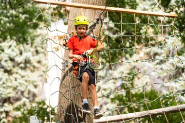 Yüksek telli parka tırmanma macerası. Küçük çocuk dağ kaskı ve güvenlik ekipmanlarıyla rotasında ilerliyor.