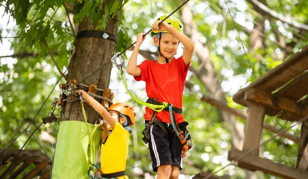 Bonito menino da escola desfrutando de um dia ensolarado em um parque de atividades de aventura de escalada — Fotografia de Stock