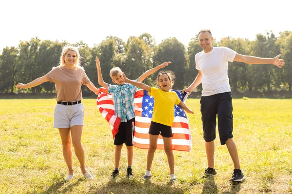 Padres y niños con bandera americana están jugando con una cometa de colores. madre, padre y sus hijas celebran juntos el 4 de julio al aire libre en un día de niebla. Concepto del Día de la Independencia de EE.UU.. — Foto de Stock