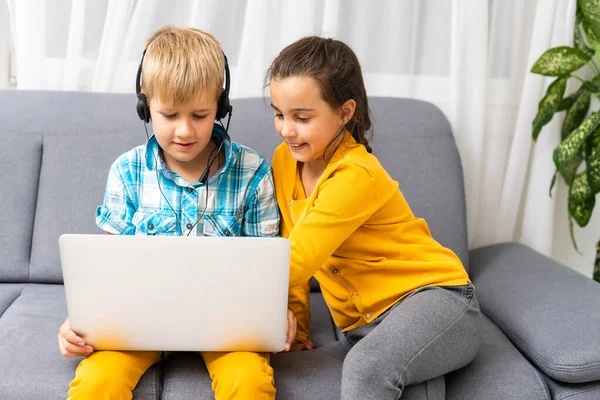 Technologie, bkids vriendschap en communicatie concept - twee schattige tieners met behulp van tablet en laptop tijdens het zitten op de bank in de woonkamer thuis — Stockfoto