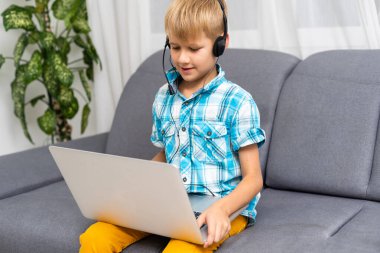 Kulaklıklı küçük beyaz çocuğun görüntüsünü kapat ve evdeki video konuşmasında konuş. Kulaklıklı küçük bir çocuğun uzaktan çekilmiş portresi bilgisayar hakkında sanal bir ders içeriyor.