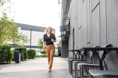 Güzel kadın ofis binası yürüyüş kahve ile çalışma olacak. İş için yolda elinde sıcak bir içecek fincan şehir sokak üzerinde tutan başarılı iş kadın portresi.