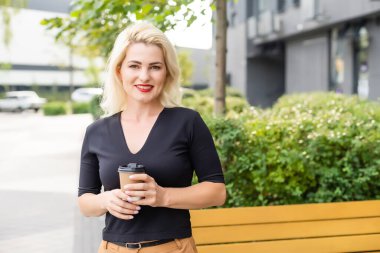 Güzel kadın ofis binası yürüyüş kahve ile çalışma olacak. İş için yolda elinde sıcak bir içecek fincan şehir sokak üzerinde tutan başarılı iş kadın portresi.