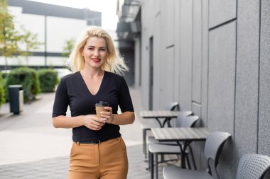 Güzel kadın ofis binası yürüyüş kahve ile çalışma olacak. İş için yolda elinde sıcak bir içecek fincan şehir sokak üzerinde tutan başarılı iş kadın portresi.