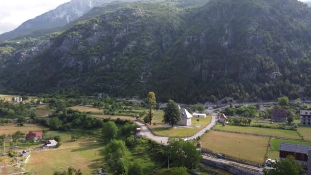 Volo vicino a vecchia chiesa di legno e alberi nella valle di Thethi, Albania. Veduta aerea del Parco Nazionale Theth, Alpi albanesi. Villaggio, fiume e montagne rocciose sullo sfondo. — Video Stock