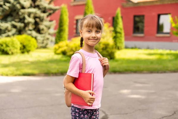 Zpátky do školy. Vzdělávací koncept. Roztomilá usměvavá školačka na cestě do školy. Šťastná holčička drží knihy s batohem. — Stock fotografie