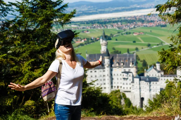 Ein Reisender mit Virtual-Reality-Brille. Das Konzept des virtuellen Reisens um die Welt. Im Hintergrund Schloss Neuschwanstein. Zukünftiges Technologiekonzept. — Stockfoto