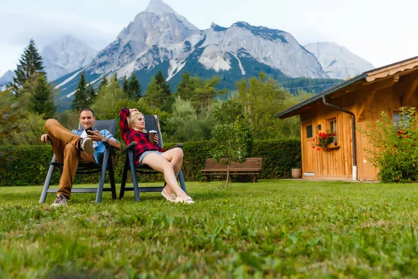 Casal feliz sentado em espreguiçadeiras na montanha Família, viagens, turismo e conceito de pessoas. Férias relaxar o tempo na natureza com a luz solar. — Fotografia de Stock