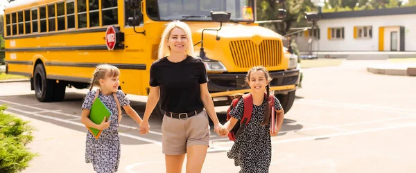 Torniamo a scuola. Gli alunni della scuola primaria vicino scuolabus. Bambini felici pronti a studiare. bambine con mamma andare in autobus — Foto Stock