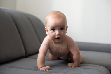 Gri bir kanepede gülümseyen şirin bir bebek.