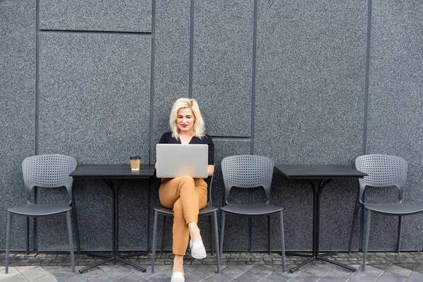 Изображение молодой красивой веселой женщины, улыбающейся во время работы с ноутбуком извне — стоковое фото