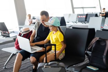 Yakışıklı baba ve küçük kızı havaalanında dizüstü bilgisayar kullanıyor.