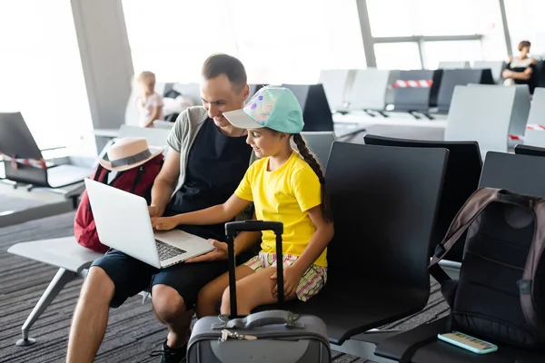 Yakışıklı baba ve küçük kızı havaalanında dizüstü bilgisayar kullanıyor.