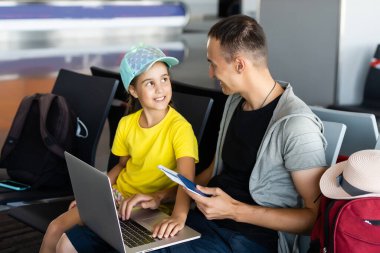 Yakışıklı baba ve küçük kızı havaalanında dizüstü bilgisayar kullanıyor.