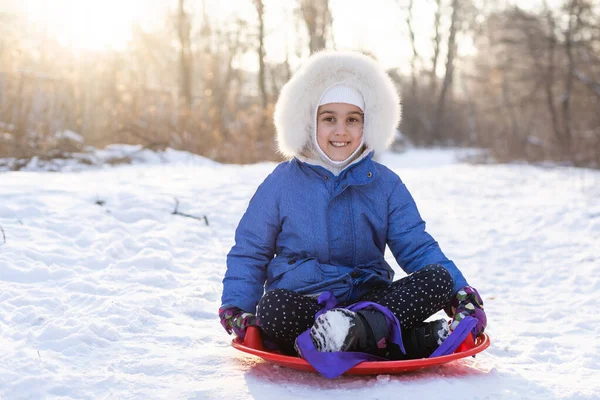 Χαριτωμένο κοριτσάκι με χειμωνιάτικα ρούχα παίζει στο πάρκο με έλκηθρα. οι χειμερινές διακοπές — Φωτογραφία Αρχείου