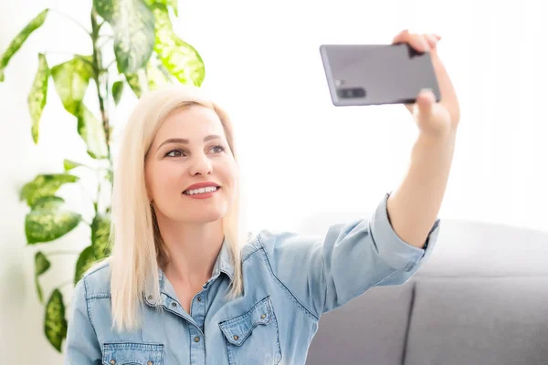 Sidovy av ung kvinna som använder smartphone vid bordet med bärbar dator — Stockfoto