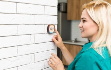 Kadın ısıyı evdeki beyaz duvara modern kablosuz termostatla düzenliyor. Akıllı ev ısıtma yönetmeliği kavramı