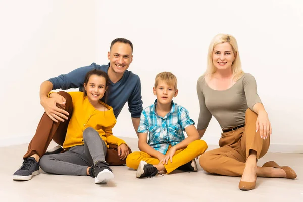 Portrait de la famille heureuse avec deux enfants assis au studio sur le plancher blanc — Photo