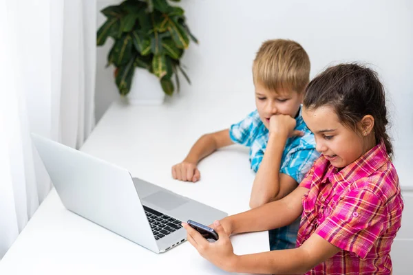 Хлопчик і дівчинка, брат і сестра навчаються вдома. Дівчинка дивиться відео урок або онлайн-конференцію, хлопчик робить вправи в блокноті з підручника — стокове фото