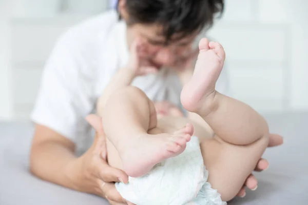 Anya és gyermek egy fehér ágyon. Anya és a kisfiú pelenkában játszanak a hálószobában. A szülők és a kisgyerekek otthon pihennek. A család jól érzi magát.. — Stock Fotó