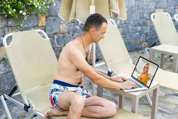 Hombre con un ordenador portátil relajante en la tumbona cerca de la piscina —  Fotos de Stock